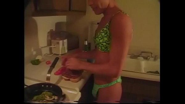 Tanned gay in lingerie prepares dinner in the k...