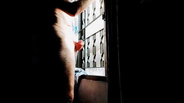 Man massaging his cock in front of a window.