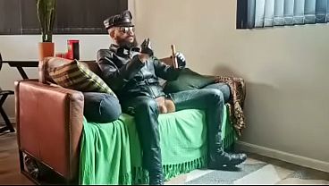 Mestre fumando um charuto na sala de estar vestido de couro e chama seu submisso obediente